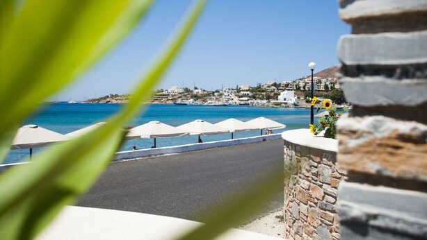 A coastal view with a stone wall, umbrellas, and a clear blue sea. - Olympia Hotel (Syros)