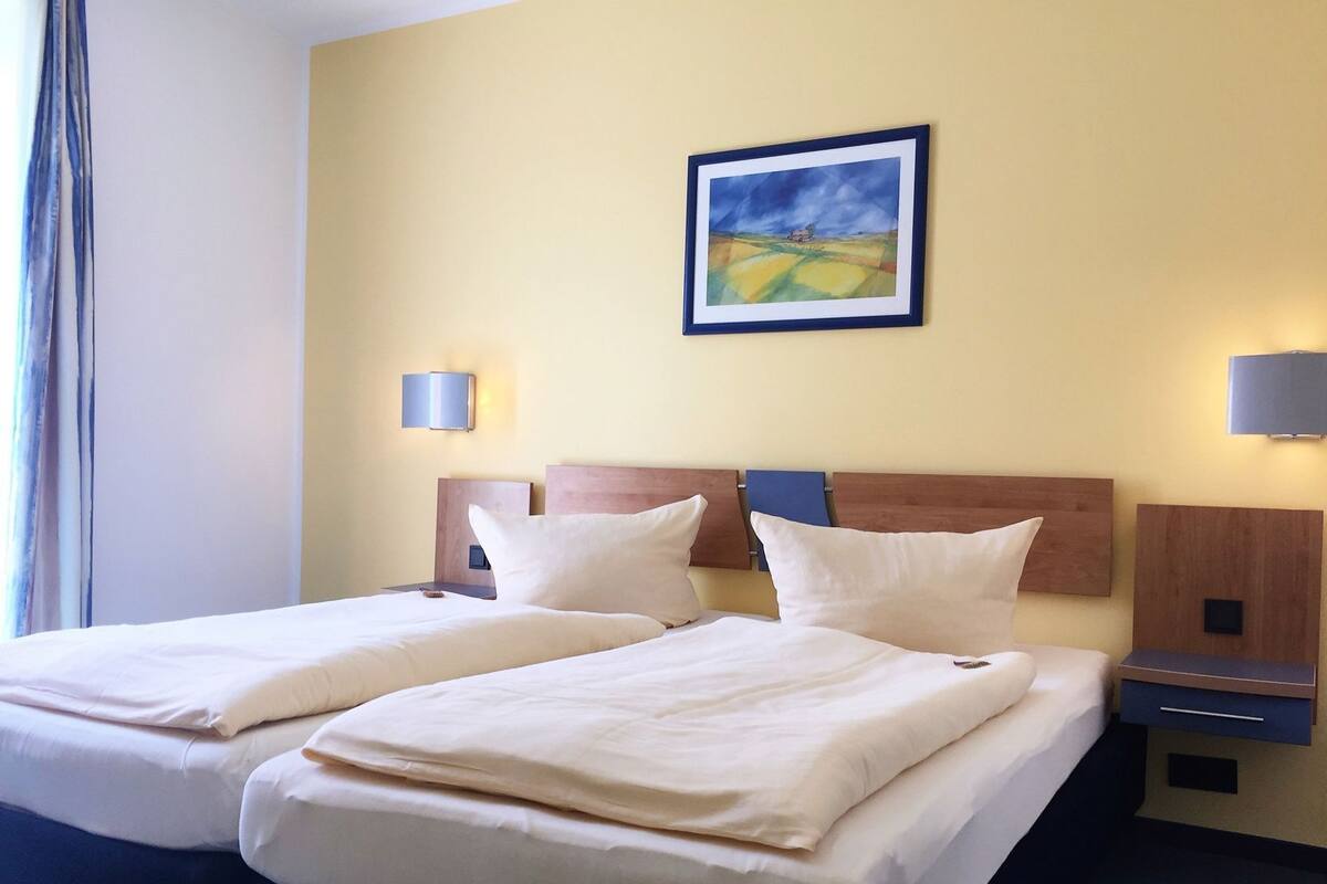 Une chambre d’hôtel avec deux lits, un tableau au mur et des lampes de chevet.