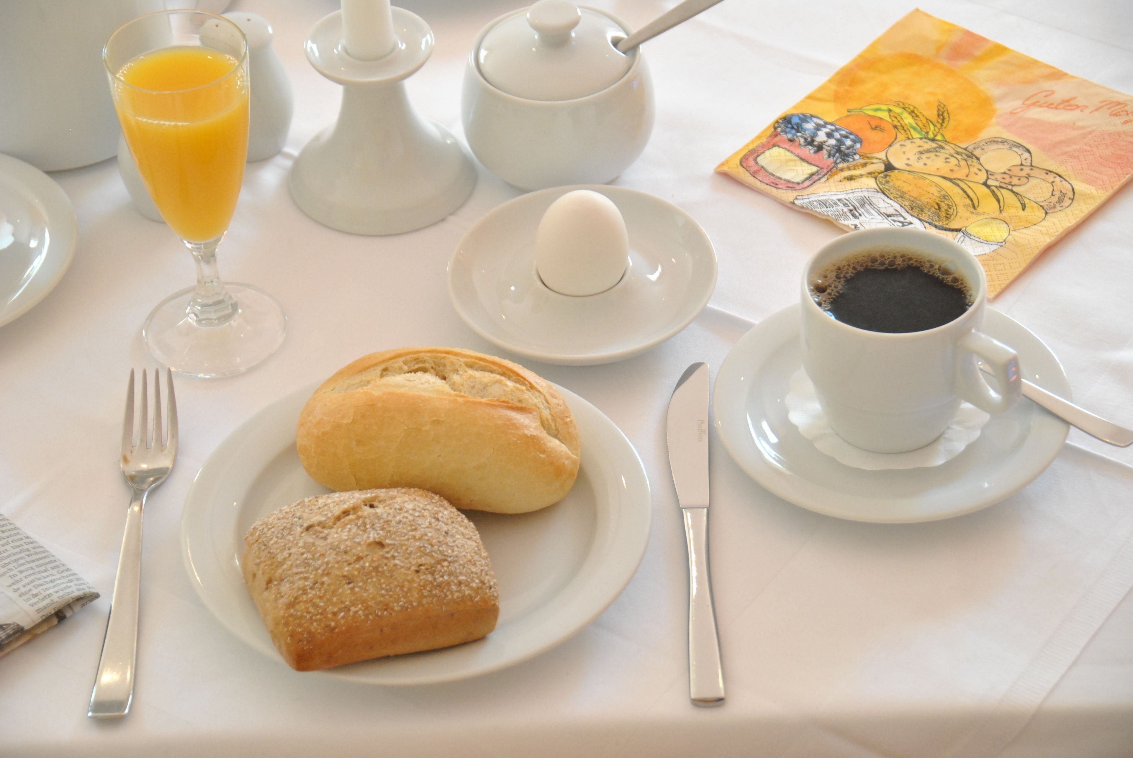 A breakfast setting with a plate of pastries, a glass of orange juice, a cup of coffee, and a teapot.