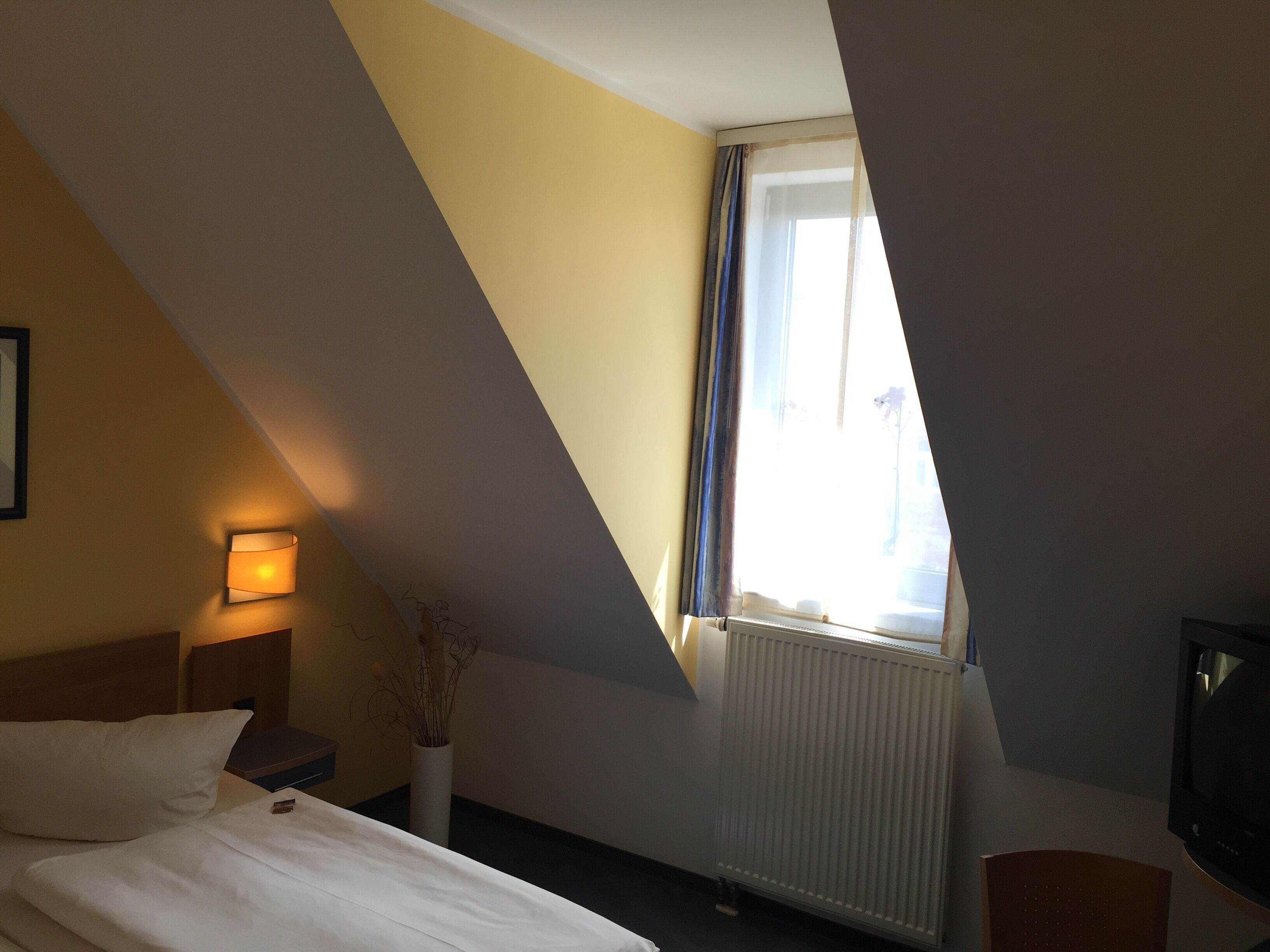 A hotel room with a bed, a bedside lamp, a radiator, and a television.