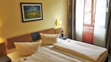 Habitación de hotel con dos camas, un cuadro en la pared, una botella de vino y una ventana con cortinas.