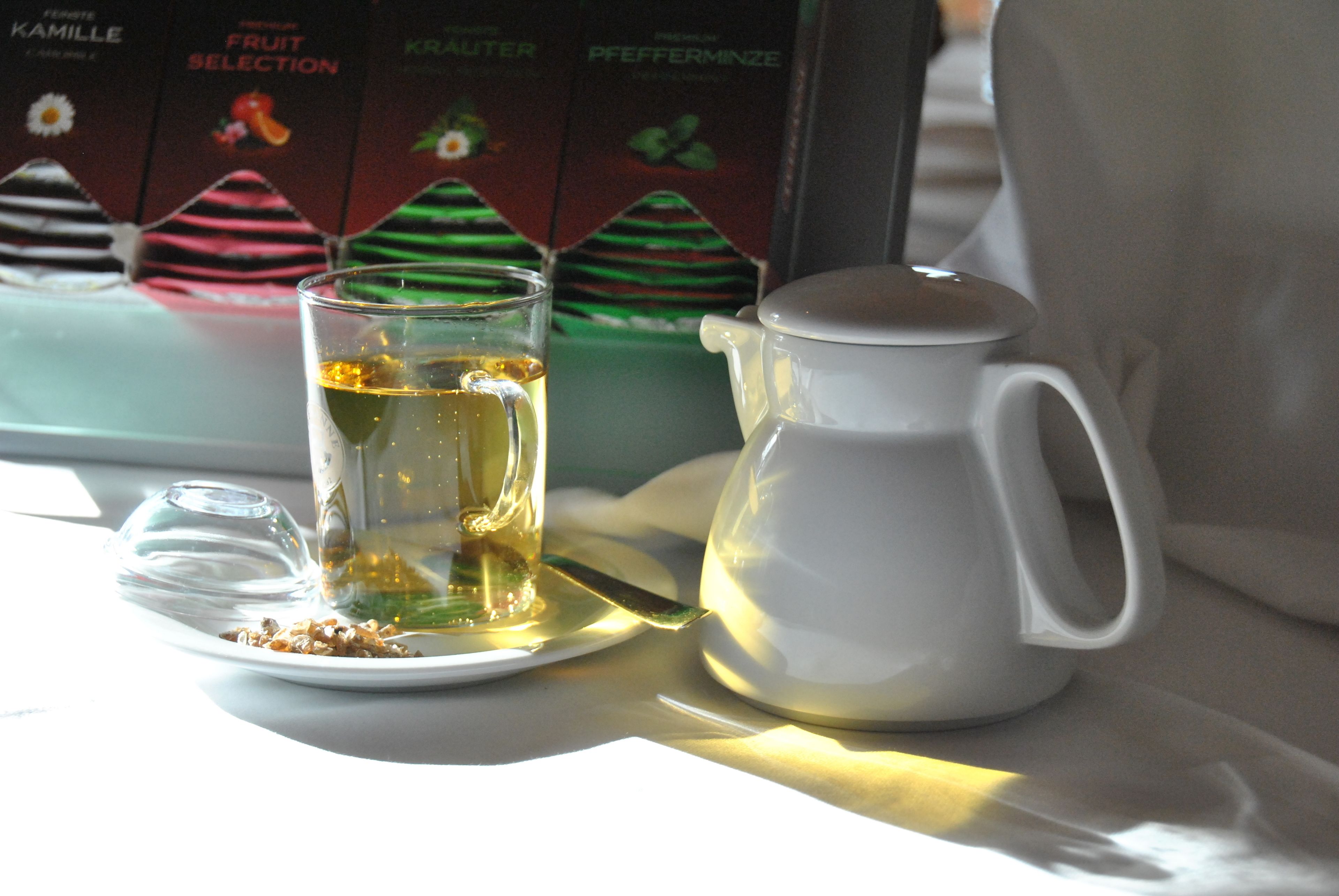 Une tasse de thé posée sur une assiette, avec une théière à côté, et un assortiment de boîtes de fruits en arrière-plan.