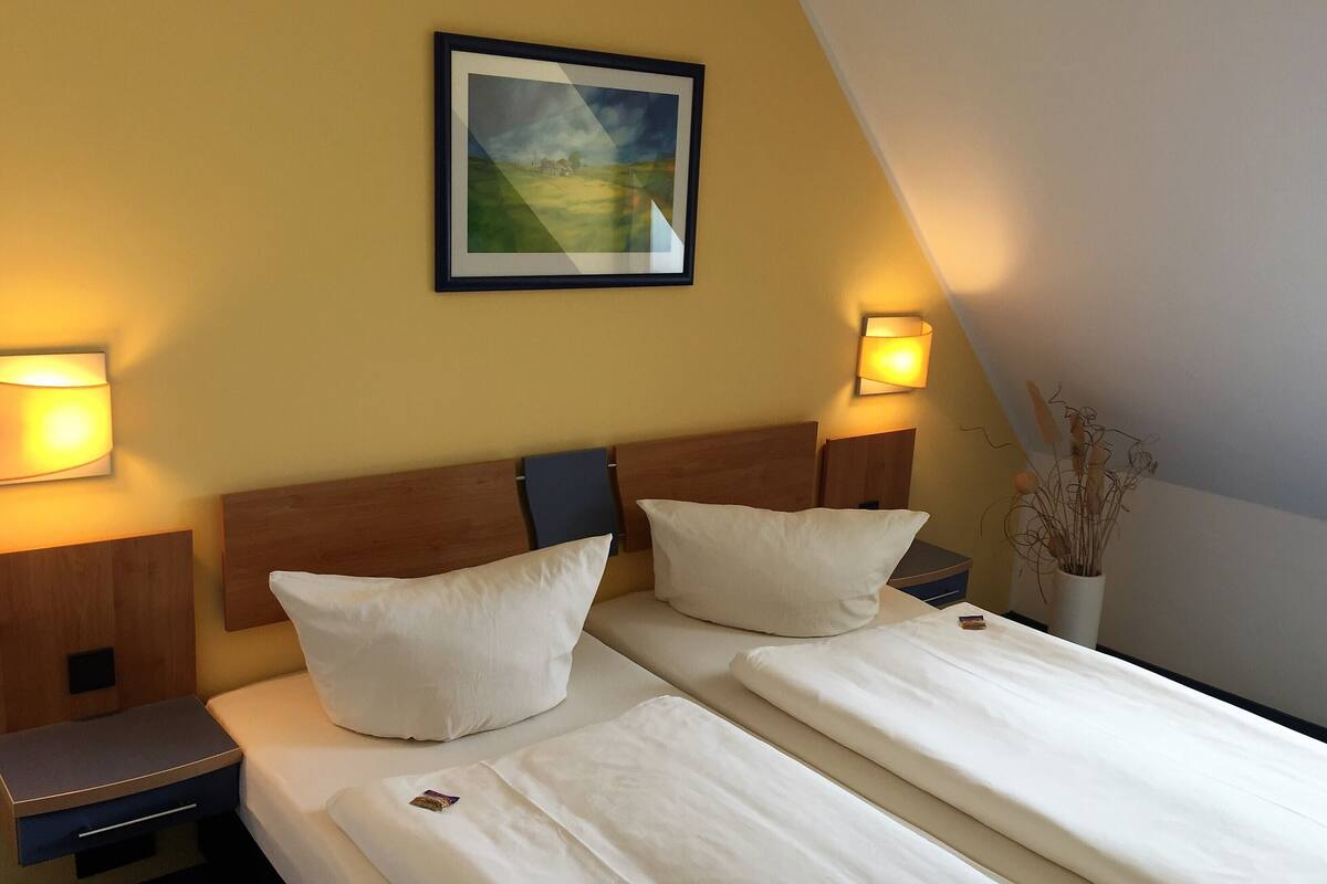 Une chambre d’hôtel avec deux lits, un tableau encadré au mur et des lampes de chevet.