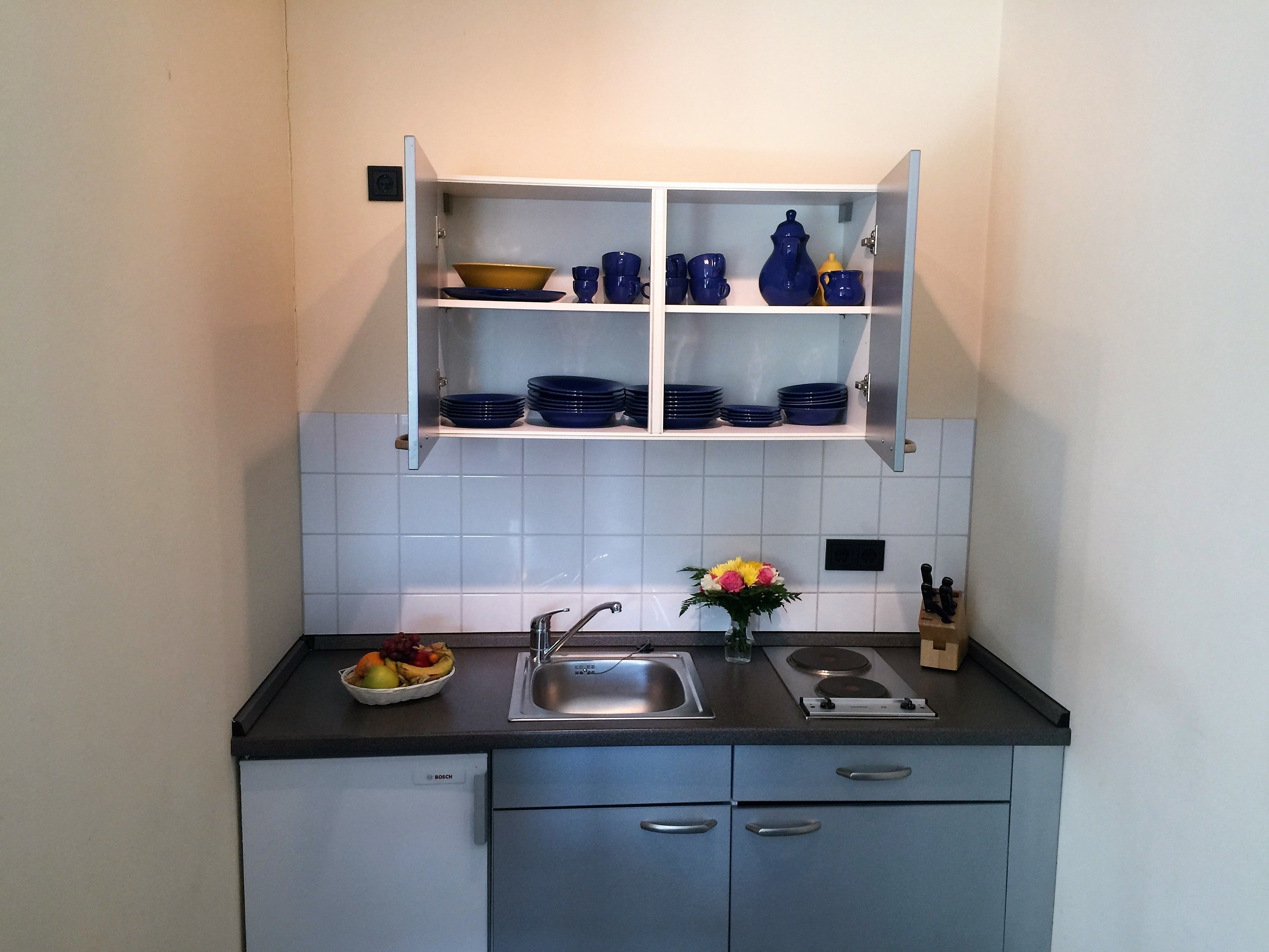 A kitchen with a Bosch refrigerator, a sink, and a cabinet with blue dishes.
