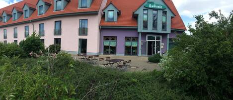 A hotel with a red-tiled roof, a green sign reading "HOTEL Ambiente", and a patio area with outdoor seating.