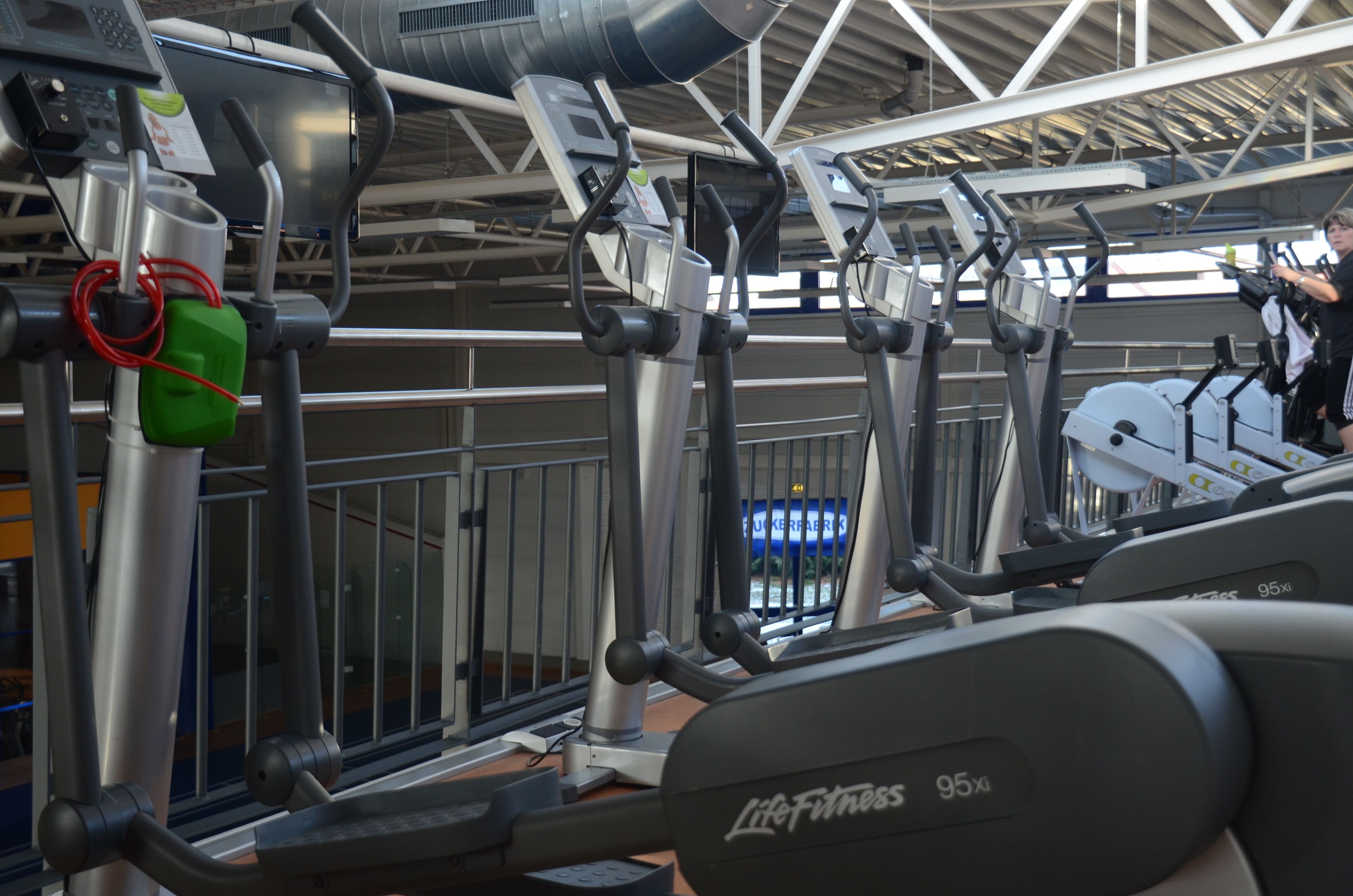 Varias cintas de correr en un gimnasio con techo metálico y vista a un edificio al fondo.