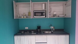 A kitchen with teal walls, white cabinets, a microwave, a coffee maker, and a sink.
