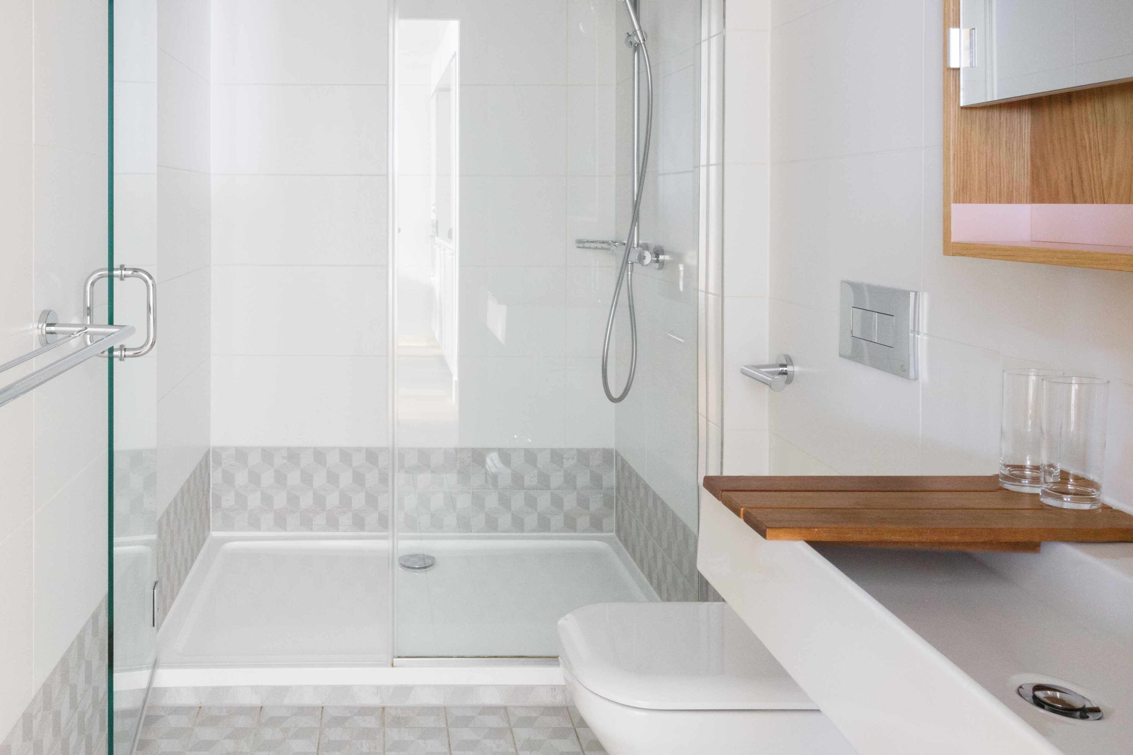 Ein modernes Badezimmer mit einer in Glas abgeschirmten Dusche, einer weißen Badewanne und einem hölzernen Waschtisch mit einer Glasablage.