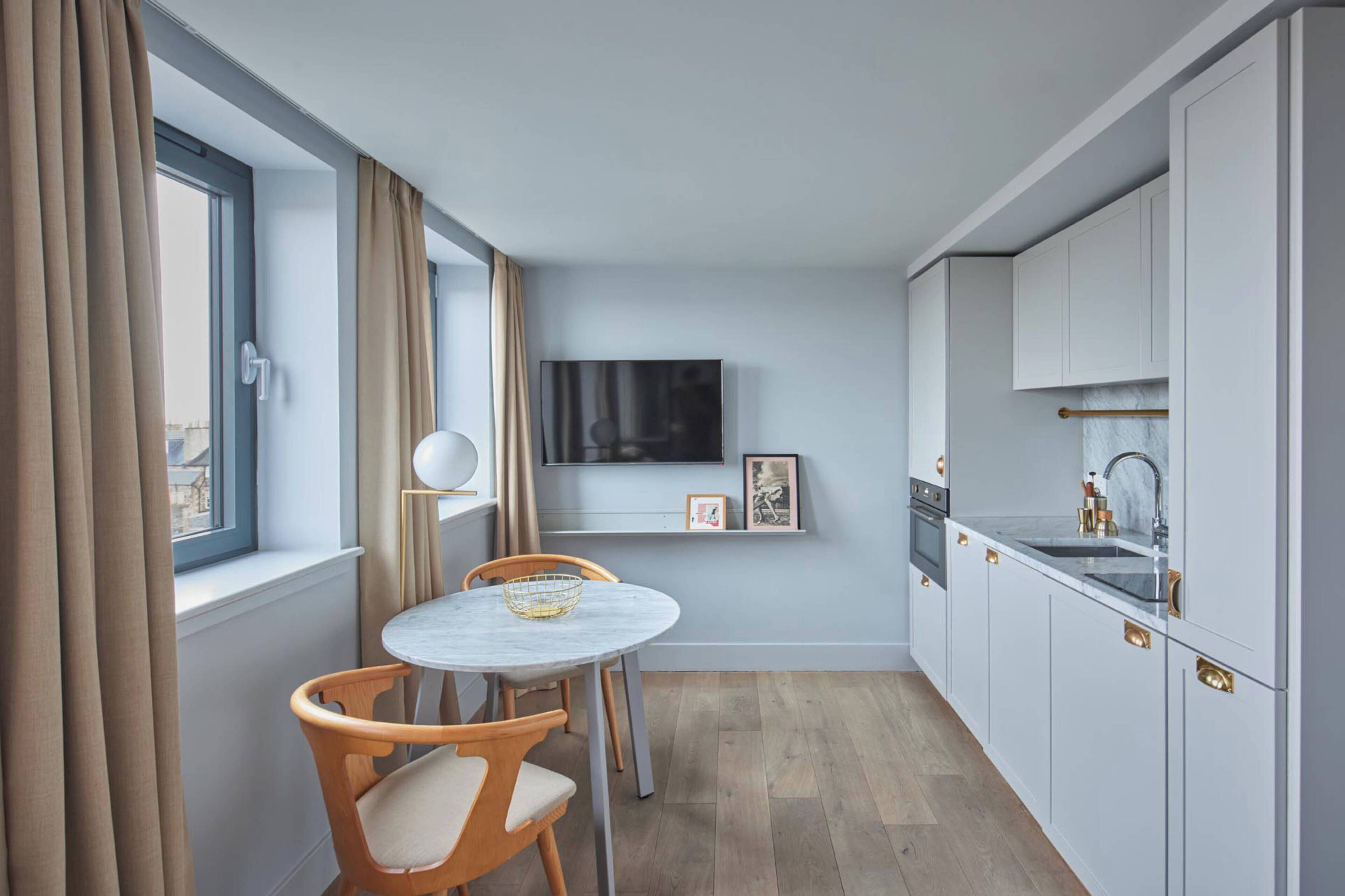 Cocina compacta con comedor, televisor sobre la encimera y ventana con cortinas.