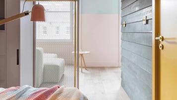 A bedroom with a bed, a desk, a chair, and a window with a mesh screen.