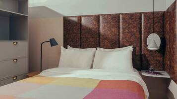 Habitación de hotel con cama, mesita de noche con lámpara, una pequeña mesa con un libro y un vaso, y un armario con espejo.