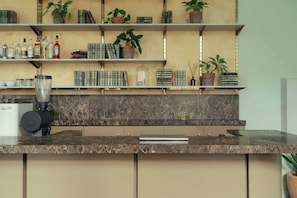 A kitchen with marble countertops, shelves with books and bottles, and a coffee machine.