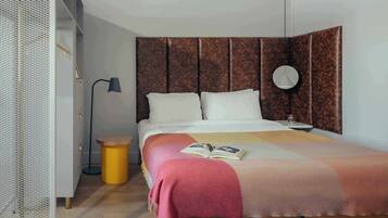 Un dormitorio ordenado con cama, mesita de noche, lámpara y un reloj de pared redondo.