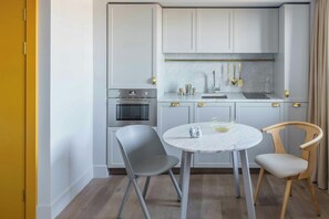 A modern kitchen with white cabinets, a marble countertop, and a round table with two chairs.