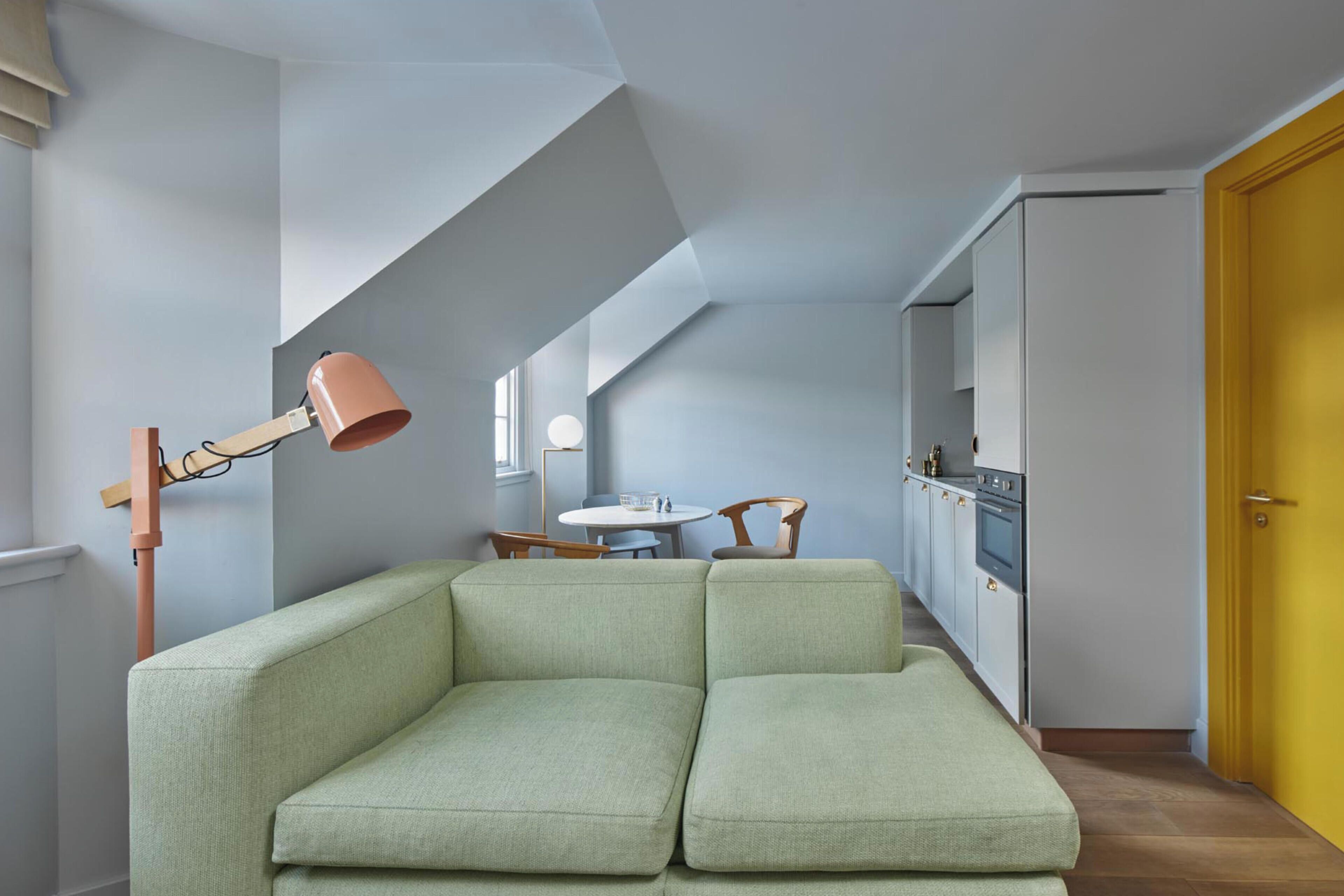 A modern interior with a green sofa, a wooden floor lamp, a kitchen area, and a yellow door.