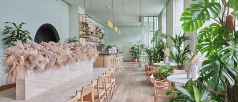 Un espacio interior amplio con una barra alargada, sillas de madera y plantas en macetas.