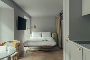 A hotel room with a bed, a TV mounted on the wall, a desk with a chair, and a window with curtains.