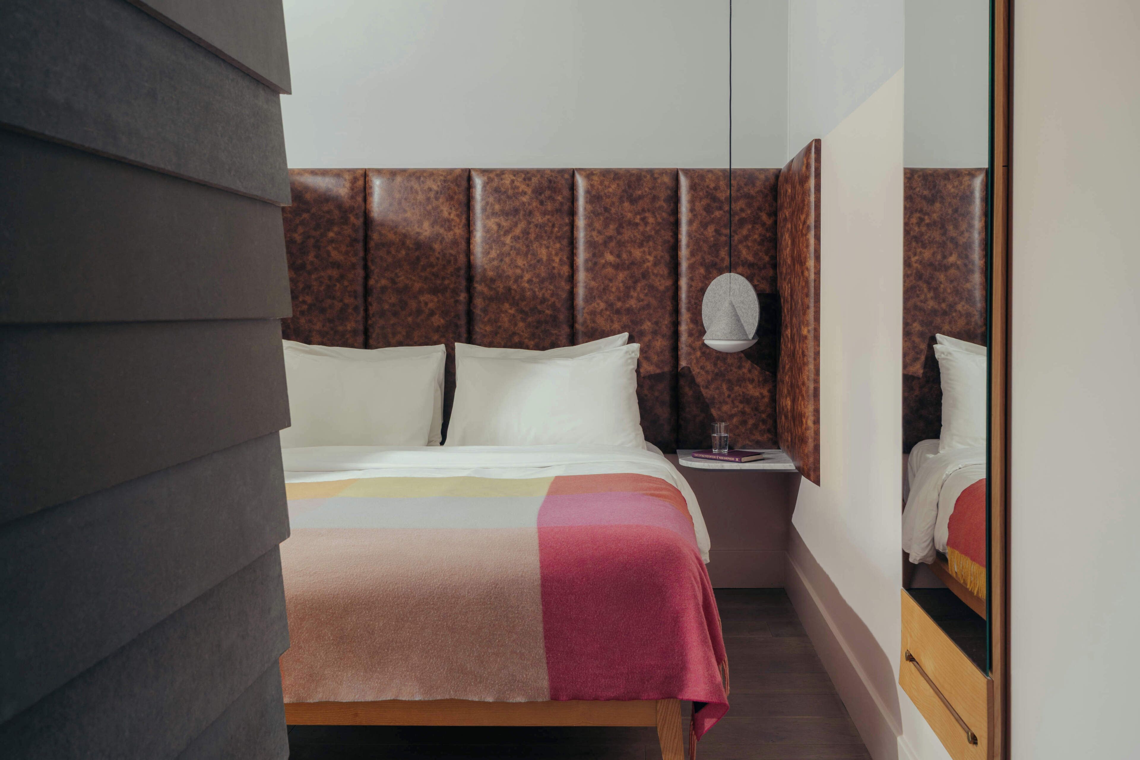A hotel room with a bed, a nightstand, a mirror, and a wall with a textured pattern.