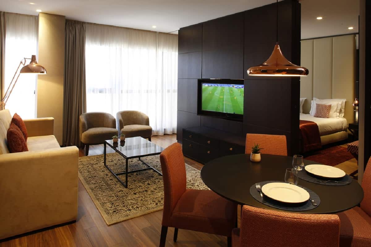 Uma sala de estar moderna com televisão, assentos confortáveis, um espaço de jantar e uma janela grande com cortinas.