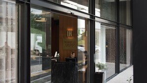 A modern hotel entrance with glass doors, a reception desk, and potted plants.
