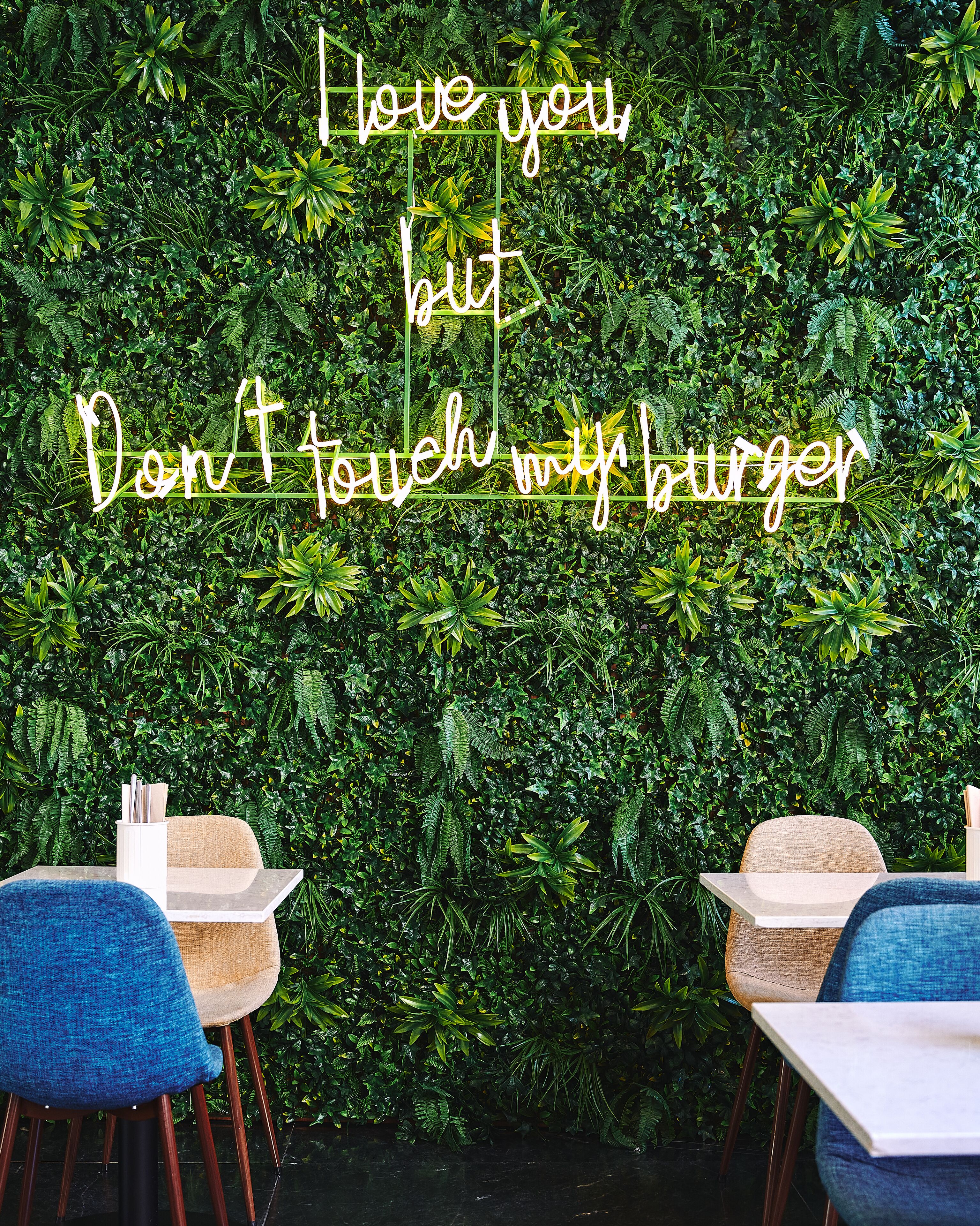 A restaurant interior with a green leafy wall and a partial view of a dining table and chairs.
