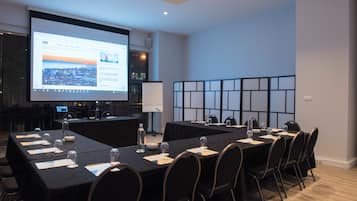Un salón de conferencias con una larga mesa, sillas, una pantalla de proyector y una pizarra.
