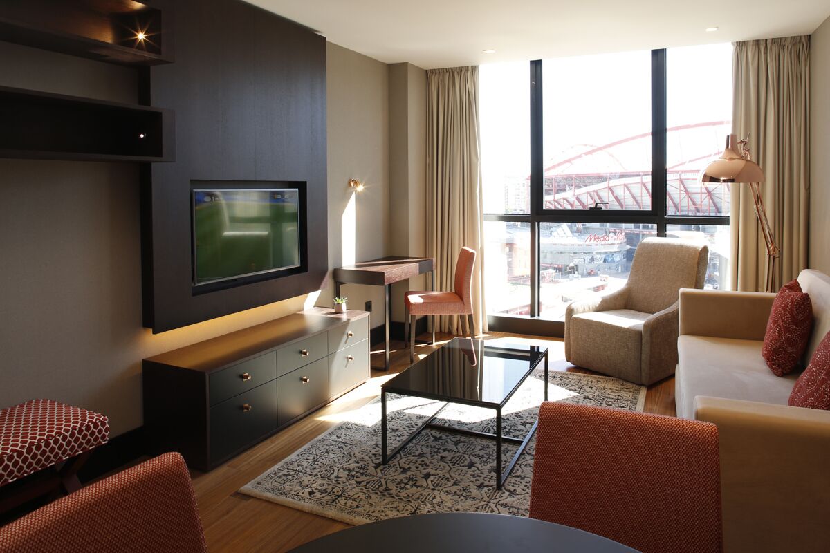 Une chambre d’hôtel moderne dotée d’une grande fenêtre, d’un téléviseur à écran plat, d’un bureau, d’un canapé confortable et d’un tapis à motifs.