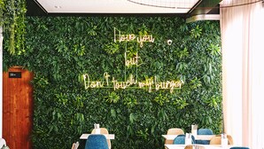A restaurant interior with a green wall, wooden furniture, and a neon sign.