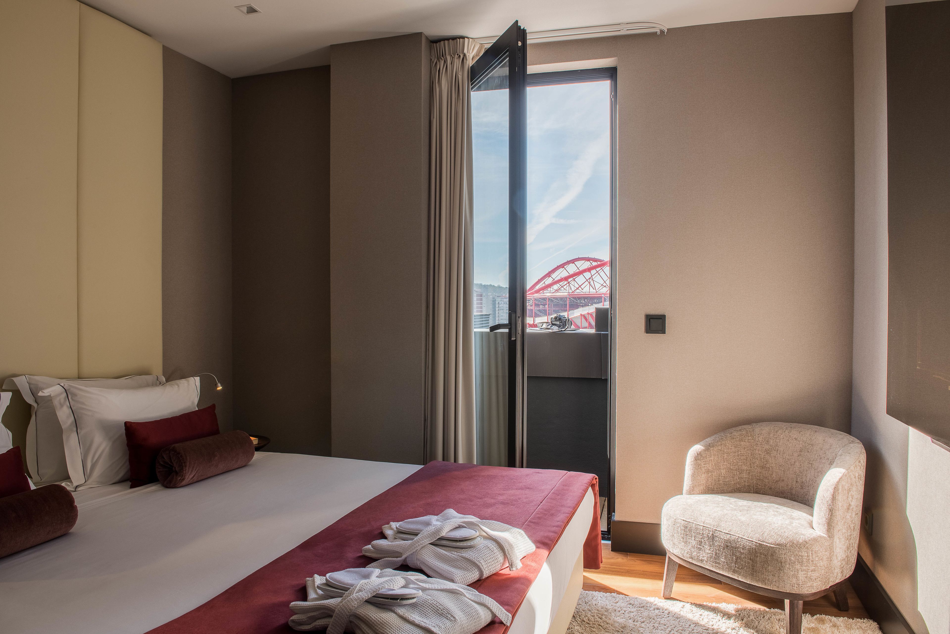 Una habitació d'hotel amb un llit, una cadira, una finestra gran i vista d'un pont vermell.