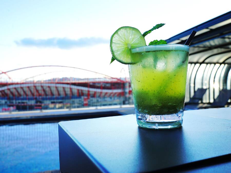 A glass of green drink with a lime slice and mint on a table with a view of a stadium in the background.