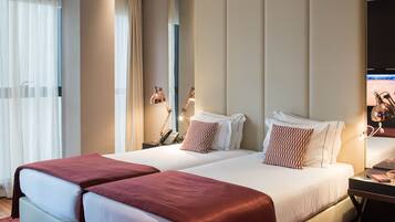 A hotel room with two beds, a desk with a lamp, a phone, and a TV on the right side.