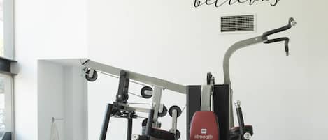 Un gimnasio con una cita motivacional en la pared, diversas máquinas de ejercicio y una ventana que proporciona luz natural.