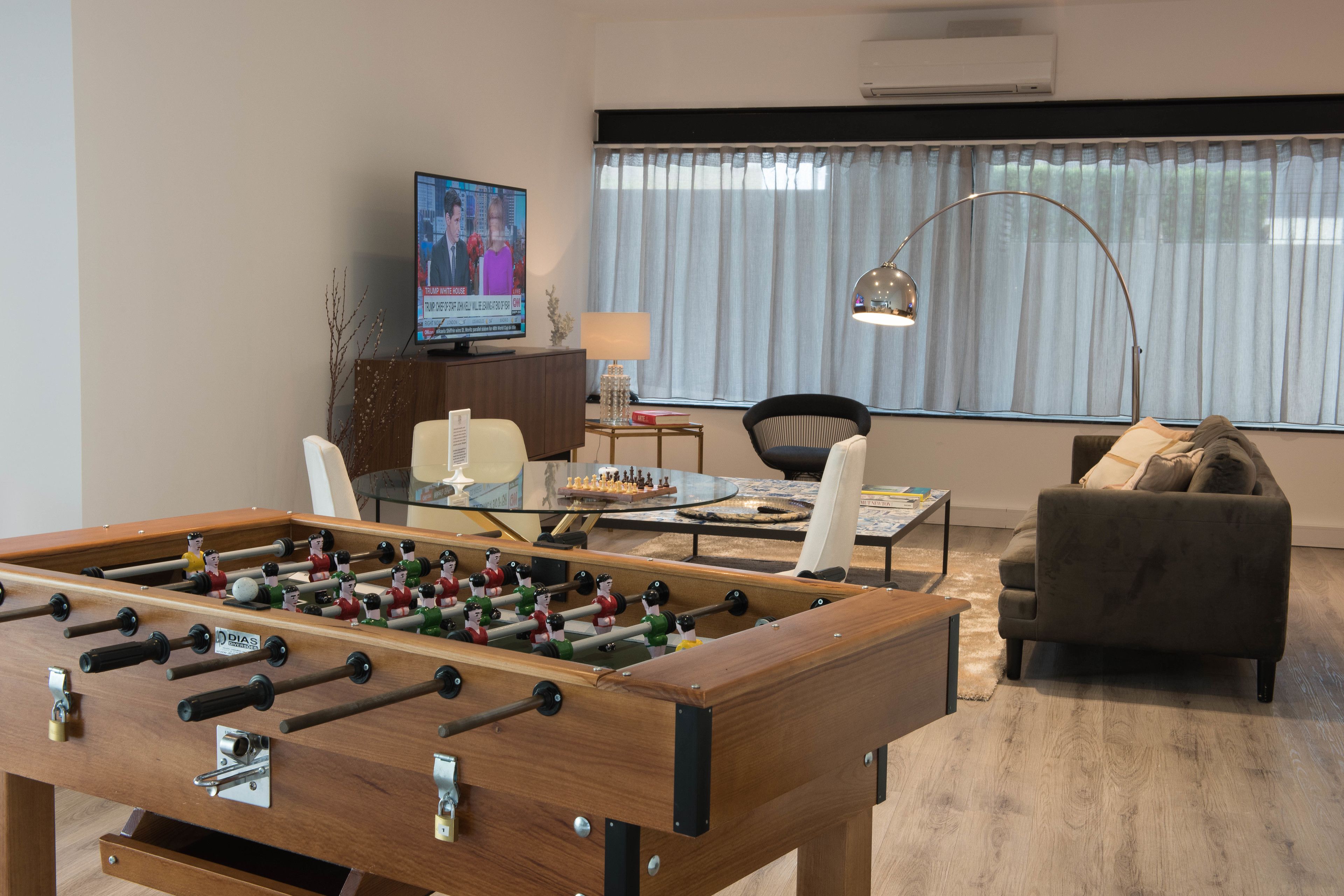 Een woonkamer met een tafelvoetbalspel, een televisie, een bank en een raam met gordijnen.