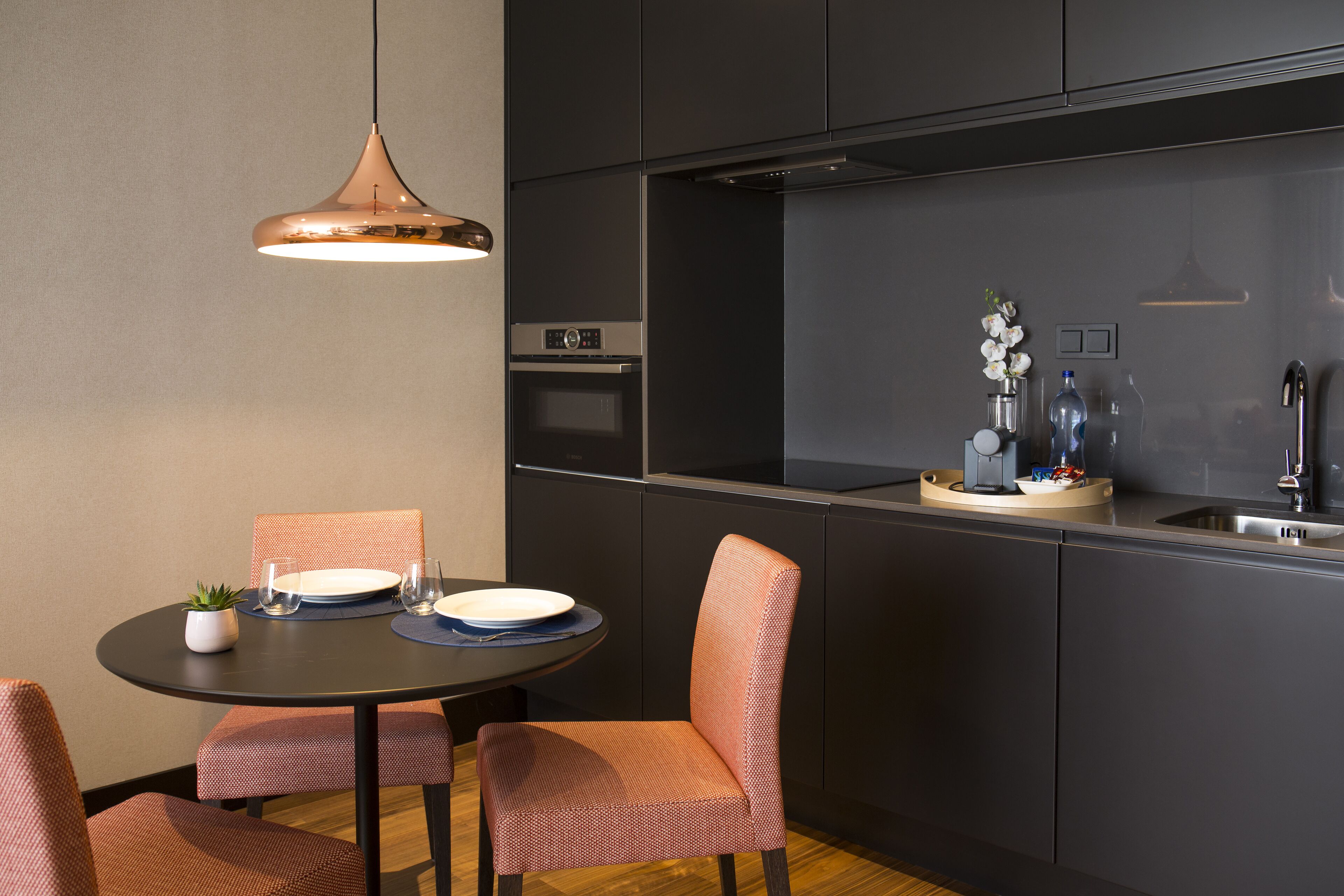 A modern kitchen with a round dining table, two chairs, a pendant light, and a built-in oven.