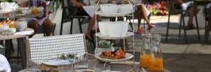 Un plateau à étages servant de présentoir, avec de la vaisselle blanche et une plante succulente, accompagné d’un verre de jus d’orange et d’un verre d’eau, le tout posé sur une table.