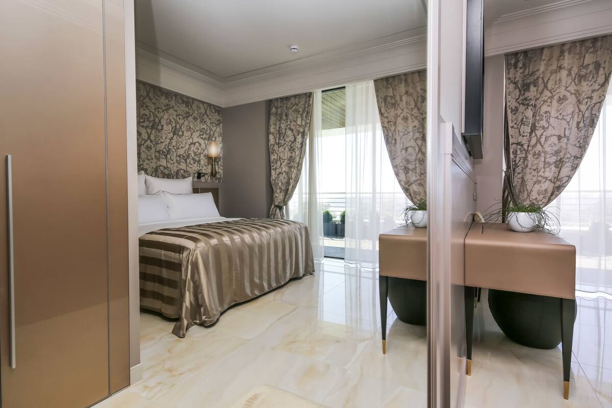 Une chambre moderne avec un lit, une coiffeuse et une grande fenêtre avec des rideaux.