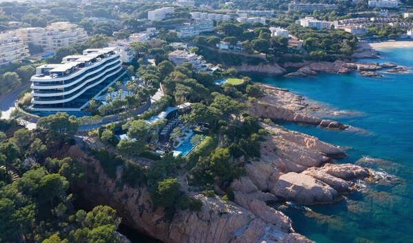 Un hôtel situé sur la côte, doté d’un bâtiment à plusieurs étages, d’une piscine et d’un terrain rocheux.
