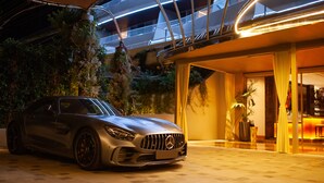 Un automóvil de lujo estacionado frente a un edificio moderno con fachada de vidrio y una zona de bar visible desde el acceso.