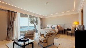 Habitación de hotel con cama, escritorio, silla, sofá, mesa de centro y vista al mar.