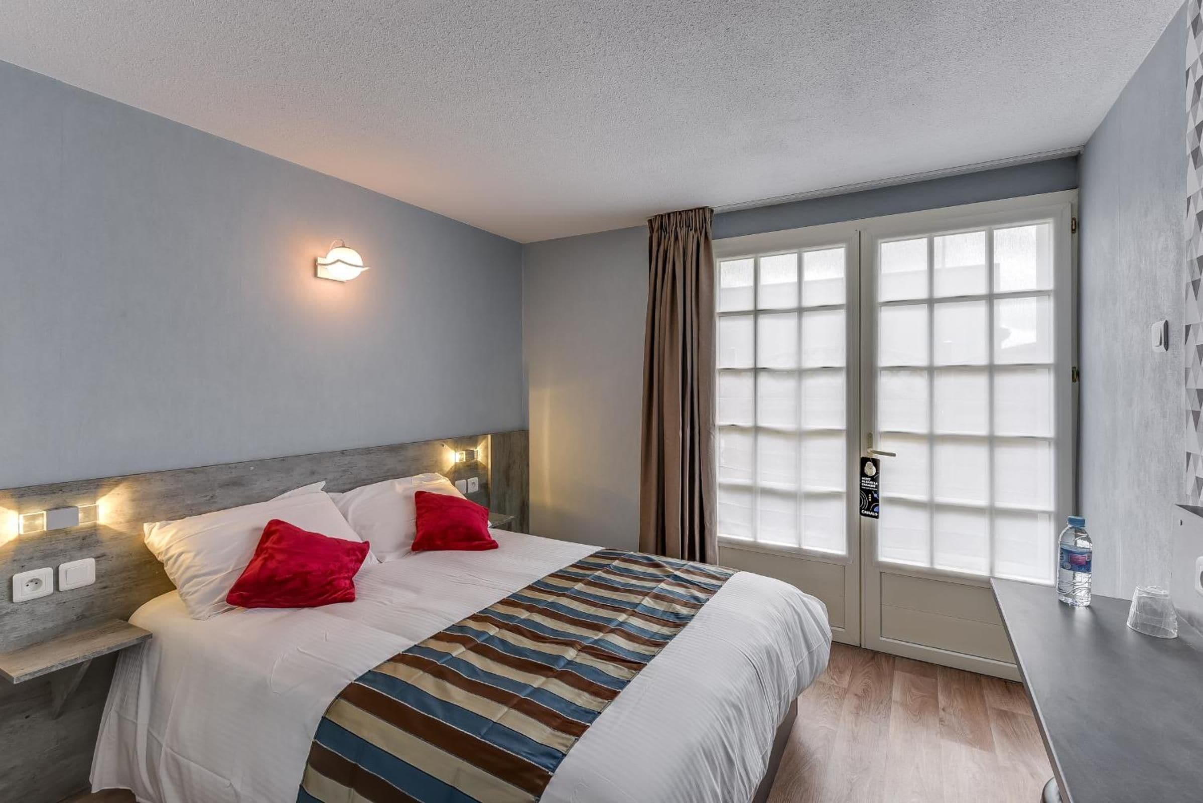 A hotel room with a bed, bedside lamps, a window with curtains, and a water bottle on the nightstand.