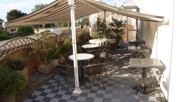 An outdoor patio with tables and chairs, a pergola, and potted plants.