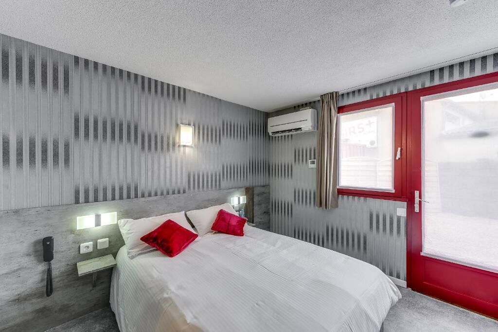 A modern hotel room with a large bed, a red door, and a view of the outside.