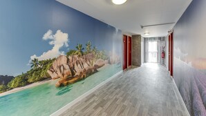 A hallway with a mural of a beach scene, wooden flooring, and red doors. - ConfortT Hotel Thouars (Thouars)