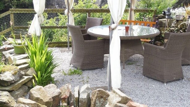 An outdoor patio area with wicker furniture, a round table, and a stone fire pit. - The Haven B&B (Castle Douglas)
