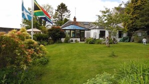 A house with a well-maintained lawn, a flagpole with flags, and a garden with various plants. - The Haven B&B (Castle Douglas)