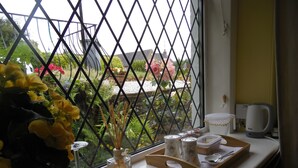 A window with a view of a garden, a table with a notebook labeled "Visitors," a bottle of perfume, and a kettle. - The Haven B&B (Castle Douglas)