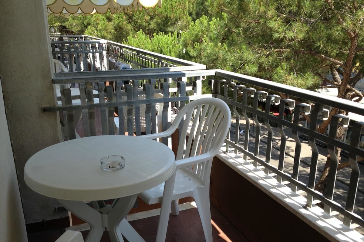 Ein Balkon mit rundem Tisch und zwei weißen Stühlen, umgeben von einem Metallgeländer.