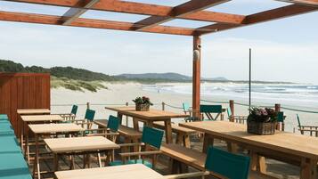 Une terrasse en bois avec des tables et des chaises donnant sur une plage.