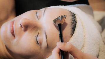 A person receiving a facial treatment with a brush and a bowl of liquid.