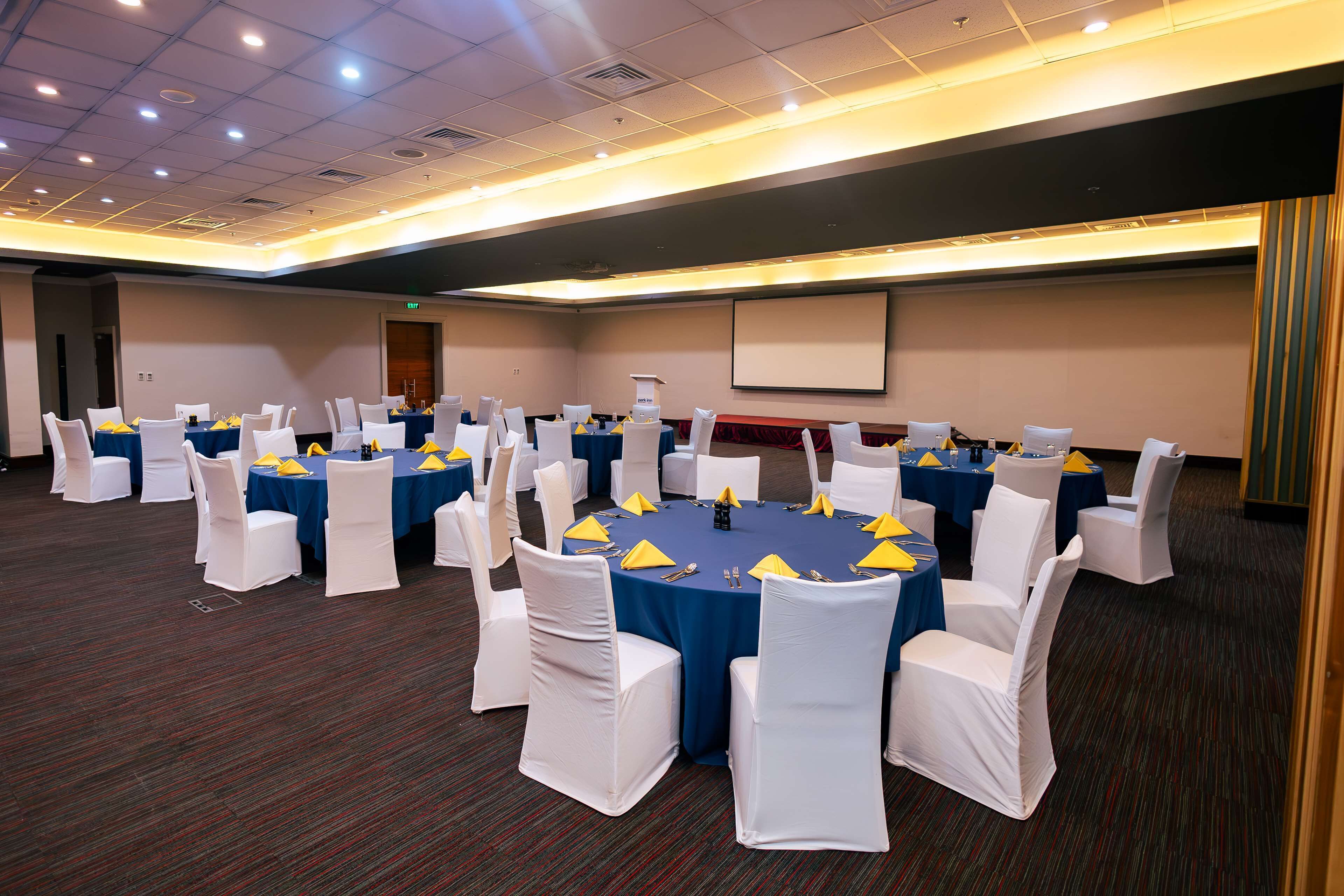 Un salón de conferencias con mesas redondas, sillas blancas y manteles azules.